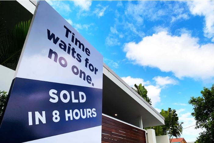 A white and blue sign outside a white-roofed house, red gate. Sign says Time waits or no one. Sold in 8 hours.