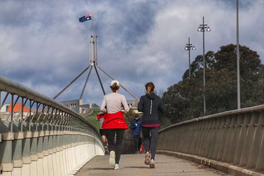 Two women run across a bridge and an australia flag flies in the background
