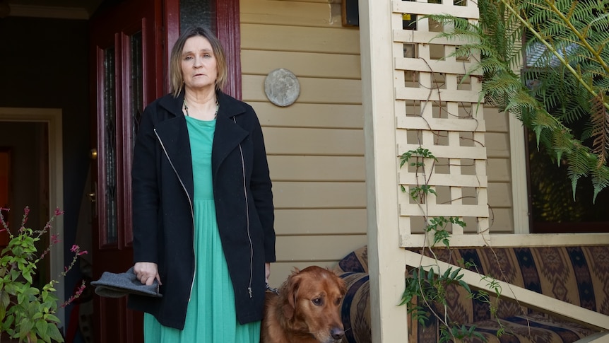 Woman with a dog standing outside her house.