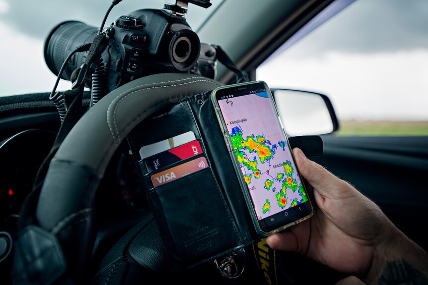 A hand holds an iPhone showing a weather radar.