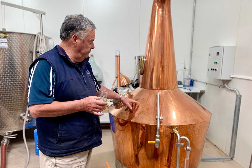 A man is touching a bronze still used for making alcohol.