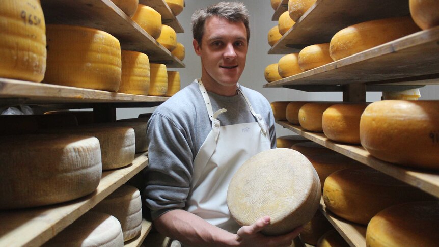 A man stands holding a wheel of cheese.