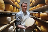 A man stands holding a wheel of cheese.