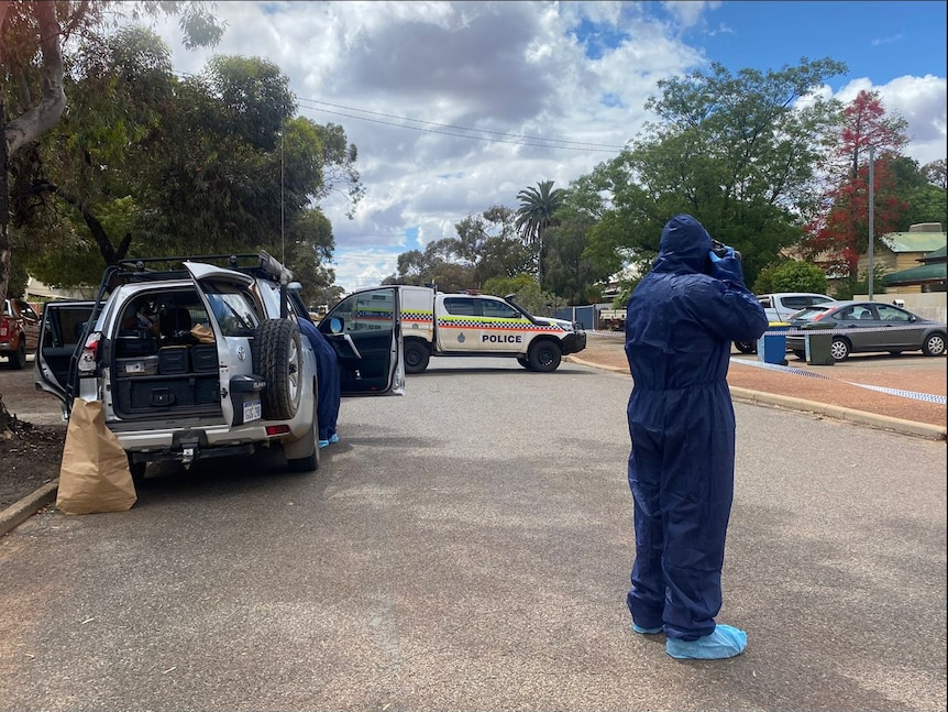 A forensic police officer in a boiler suit photographs a crime scene in Boulder, Western Australia.