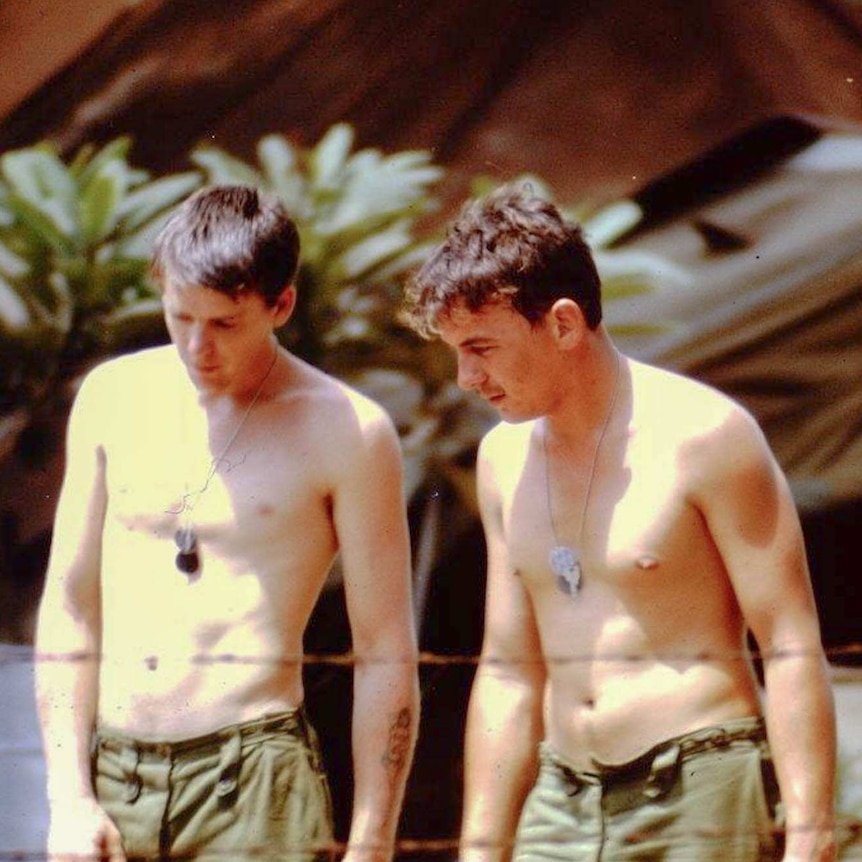 Two men standing without a shirt on wearing their tag necklaces. The photo appears to be old.