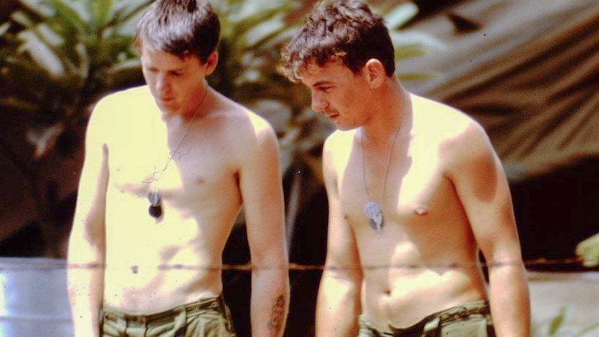 Two men standing without a shirt on wearing their tag necklaces. The photo appears to be old.