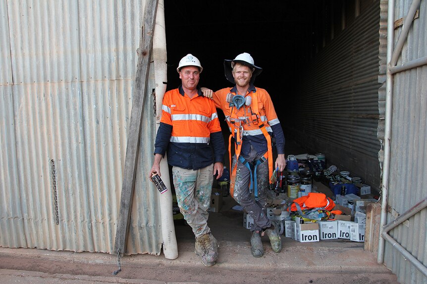 Two painters stand in the doorway of a shed smiling