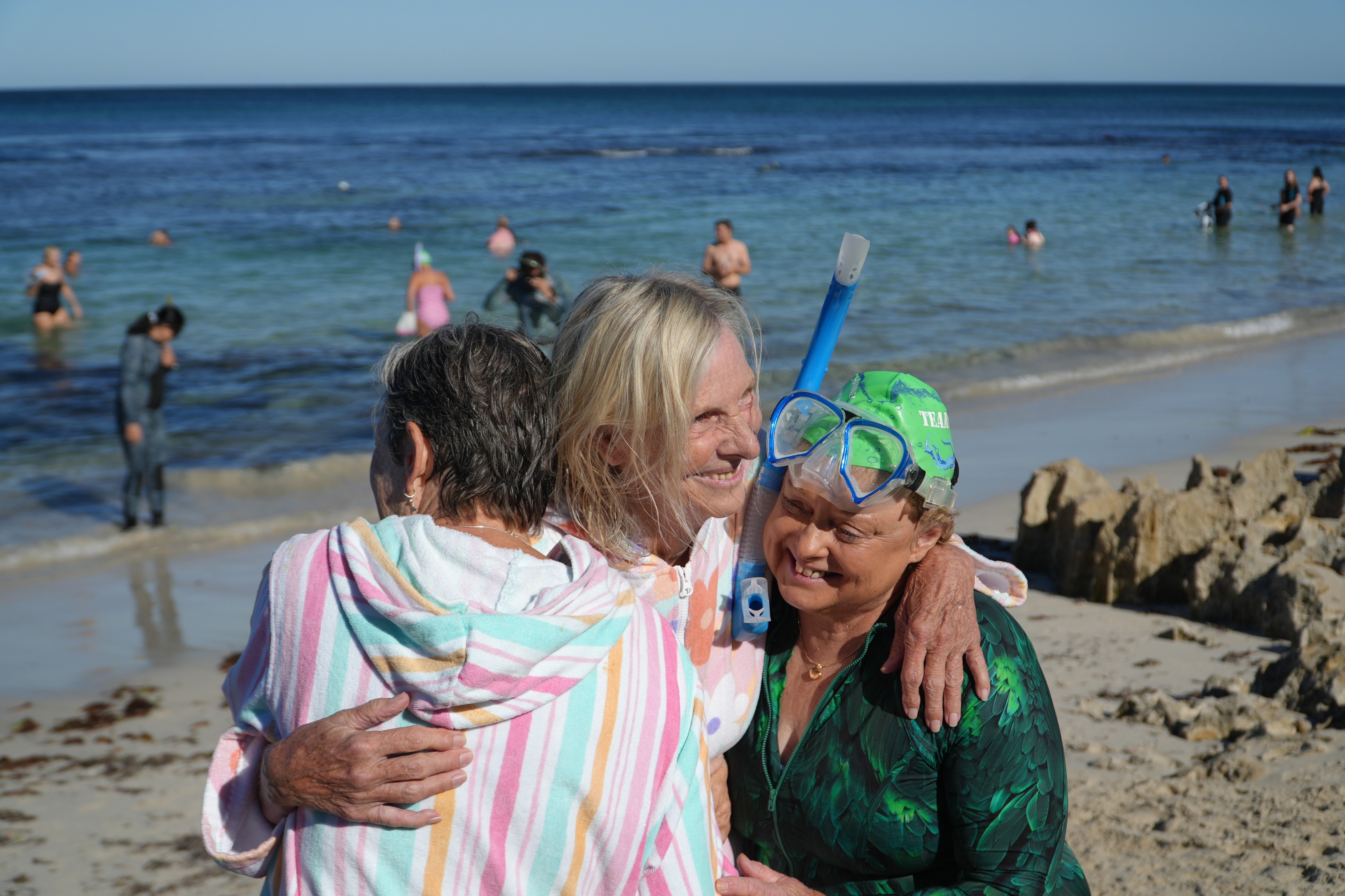 Hilly sorri enquanto abraça duas mulheres.