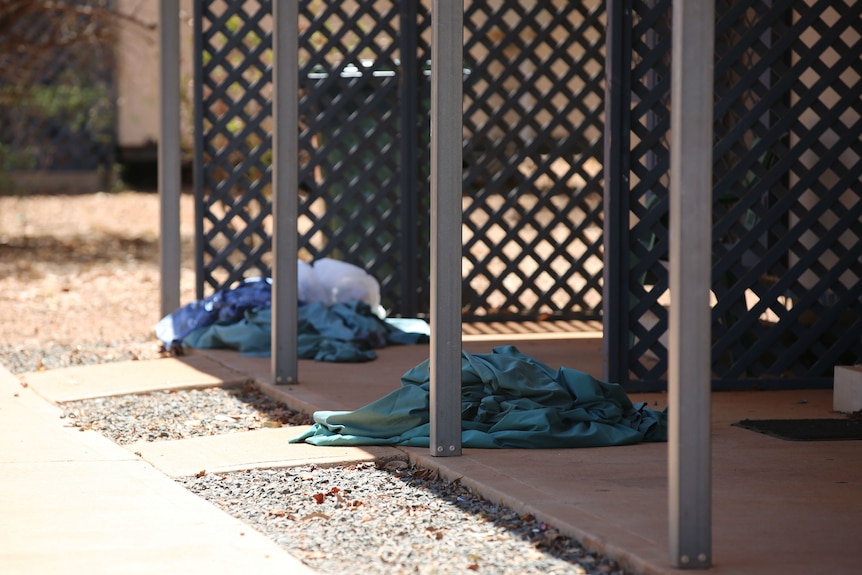 A shot of laundry on the ground of a patio with lattice and poles.