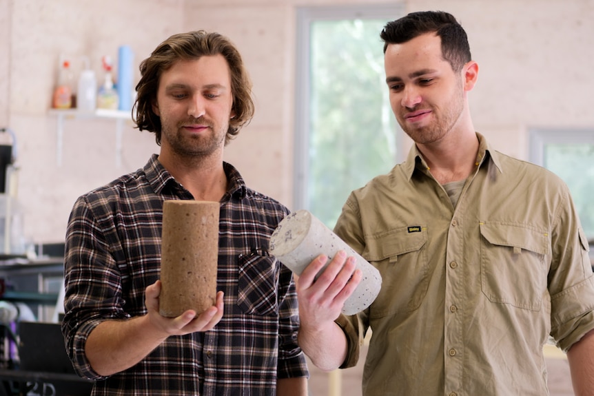 Two men looking at the small round blocks of cement they are holding in their hands