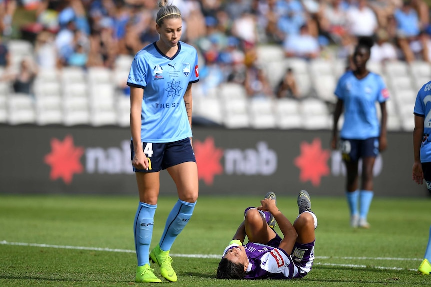Sam Kerr lies on her back holding her left ankle as Alanna Kennedy walks over to her