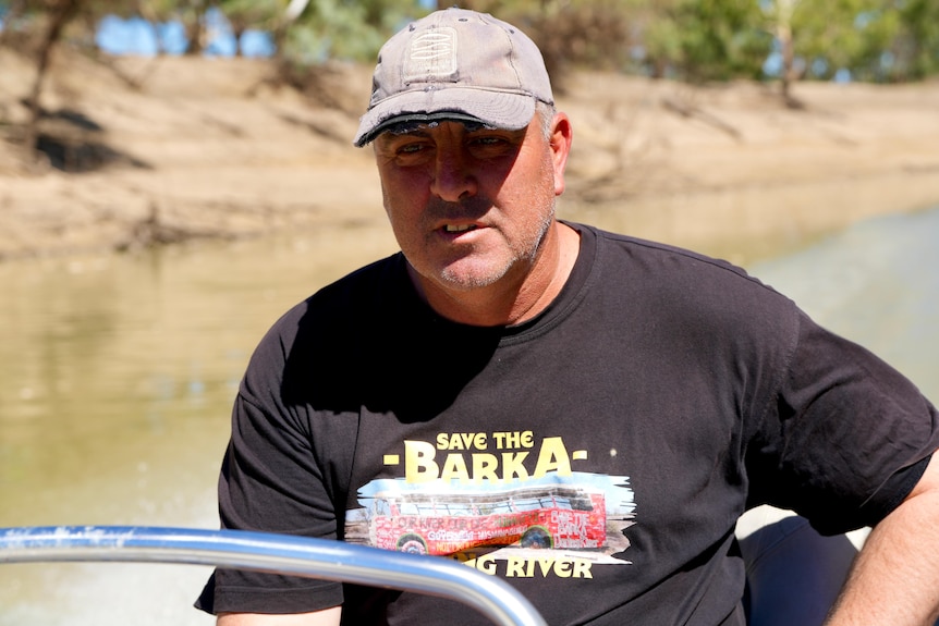 A white man wearing a black shirt driving a boat down the Darling River at Menindee