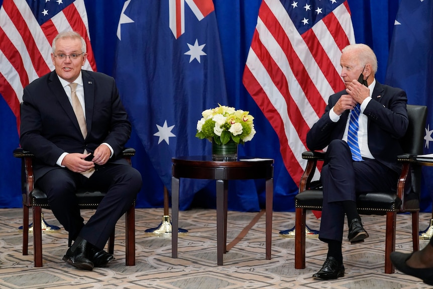 Scott Morrison places with Joe Biden in space-out chairs in front of American and Australian flags