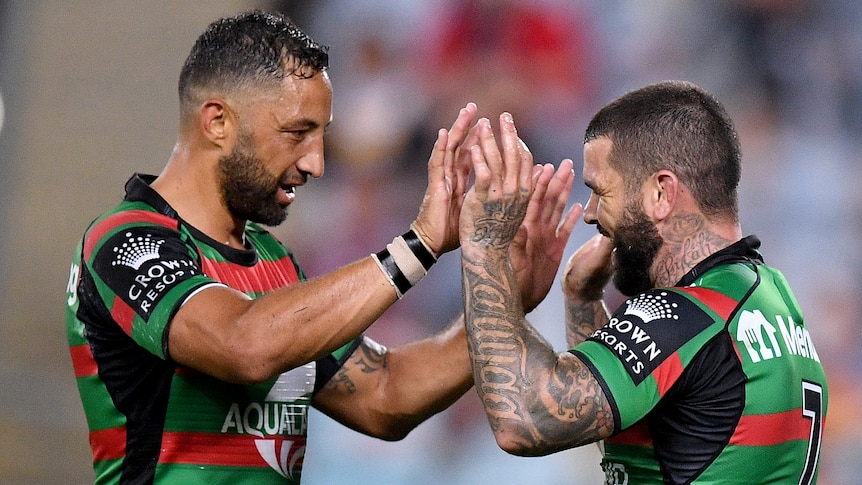 Two South Sydney NRL players touch hands as they celebrate a try against Brisbane.