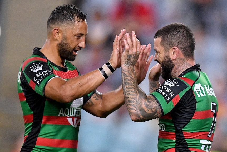 Two South Sydney NRL players touch hands as they celebrate a try against Brisbane.