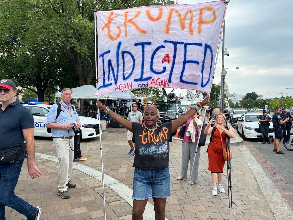 Woman holds up sign saying trump indicted again and again 
