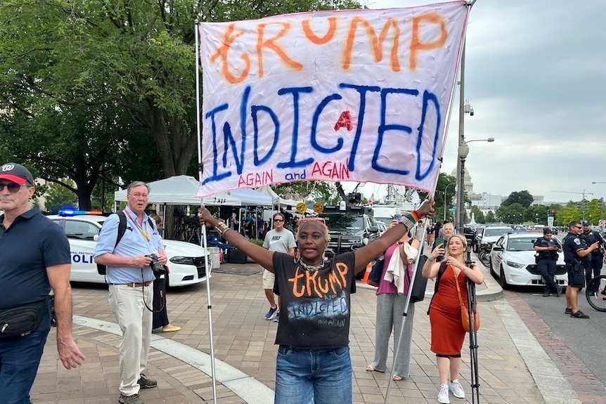 Woman holds up sign saying trump indicted again and again 