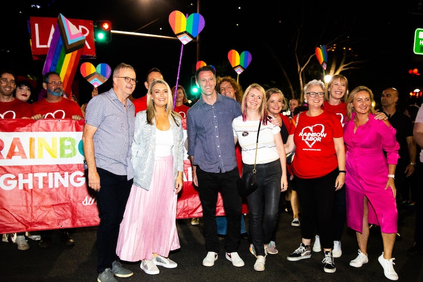 Group of people standing on street in front of rainbow banner