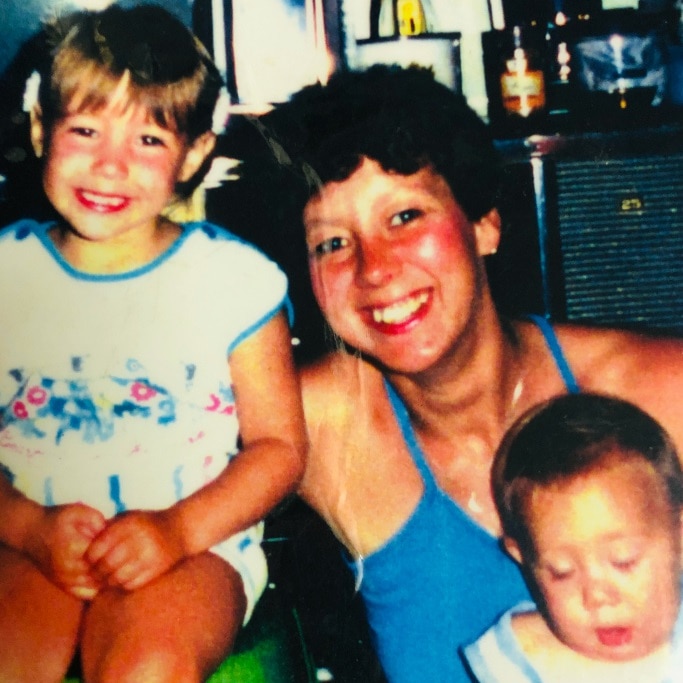 An old colour photo of a woman with a young girl and a baby