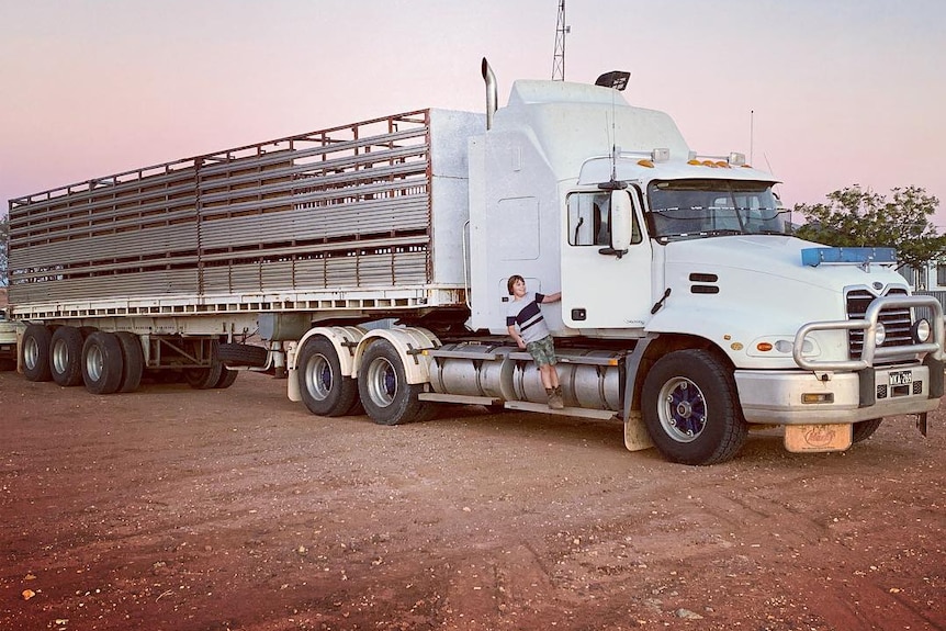 A young boy hangs on to the side of a livestock truck.