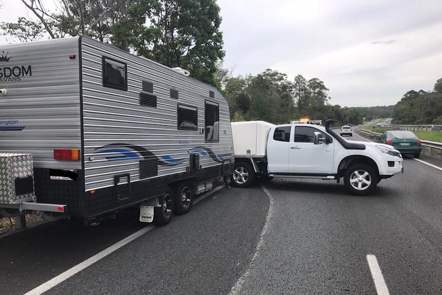 A caravan and car jackknife in the middle of a busy highway.