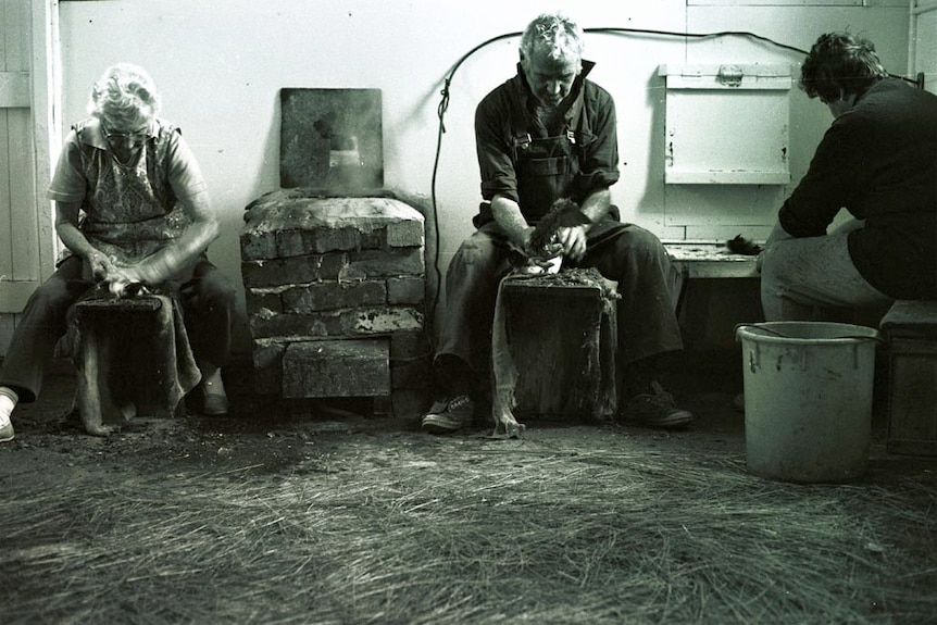 Two women and one man seated inside the birding shed, plucking feathers