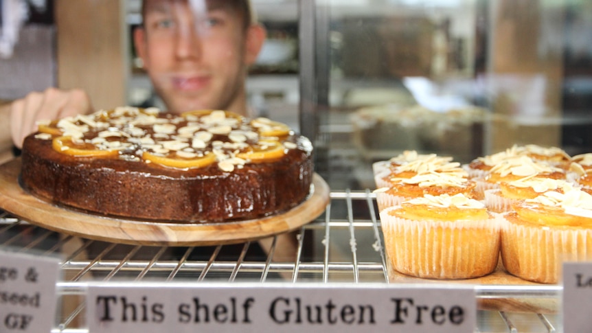 A man with short hair placing a cake in a glass cabinet.