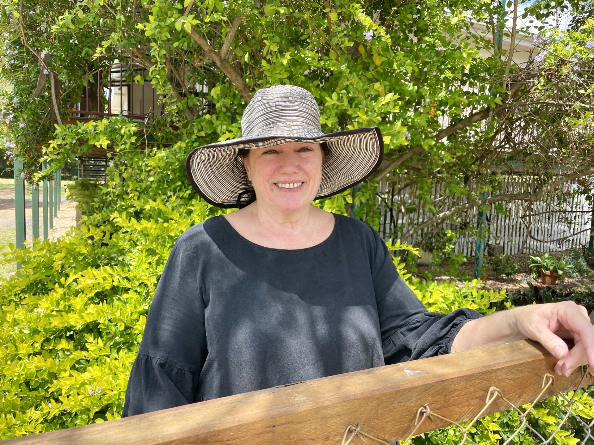 Woman wearing a wide brimmed sun hat smiling at the camera standing in her garden. 