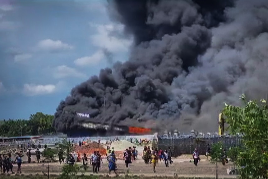 A video still shows a crowd of people outside a warehouse that is on fire 