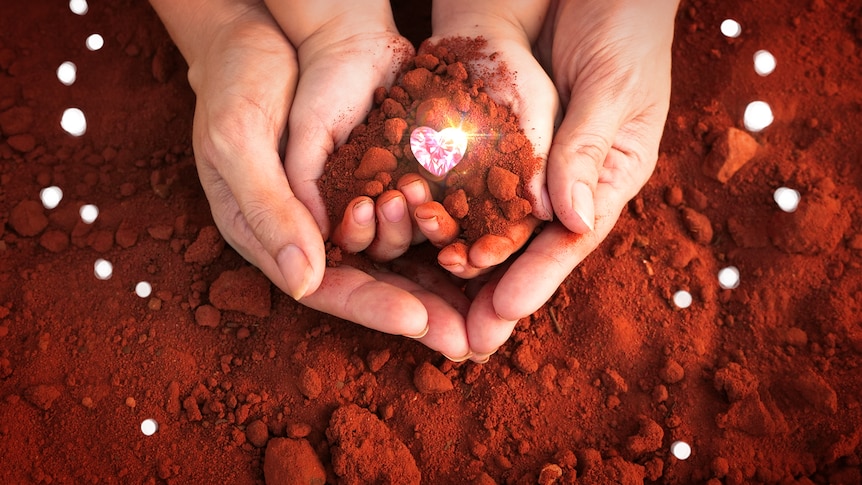 An image of a child and adult's hands holding red dirt with a superimposed picture of a pink, heart-shaped diamond.