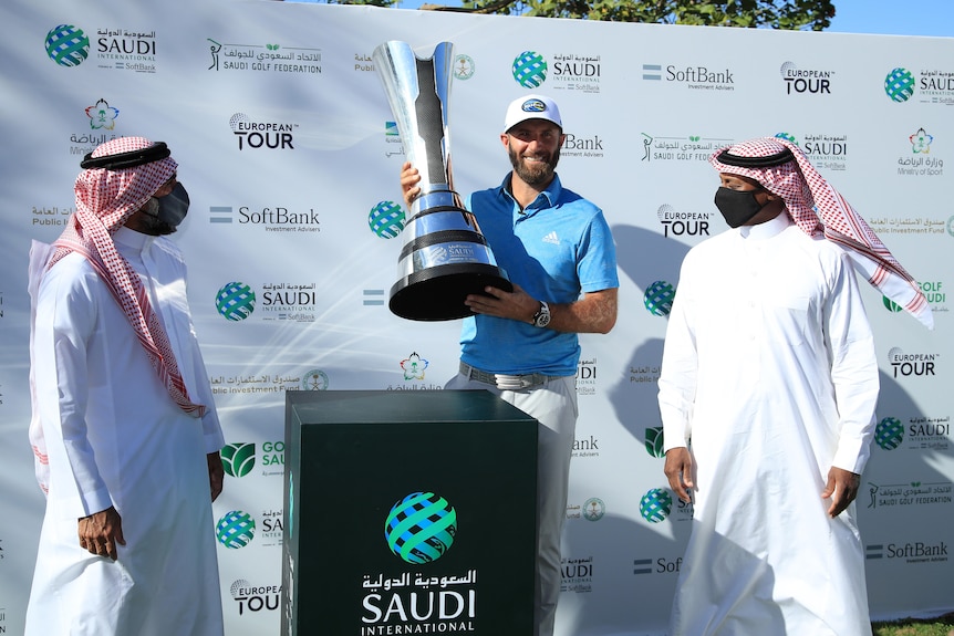 Dustin Johnson holds a trophy flanked by two men wearing traditional Saudi robes and headdresses