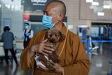 Zhi Xiang holds a small dog affectionately in his arms at the airport while wearing a face mask