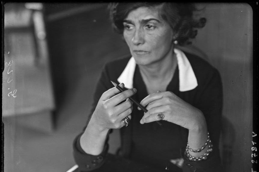 A black and white photo of a woman in her 50s with a chic hairdo and outfit holding a pen