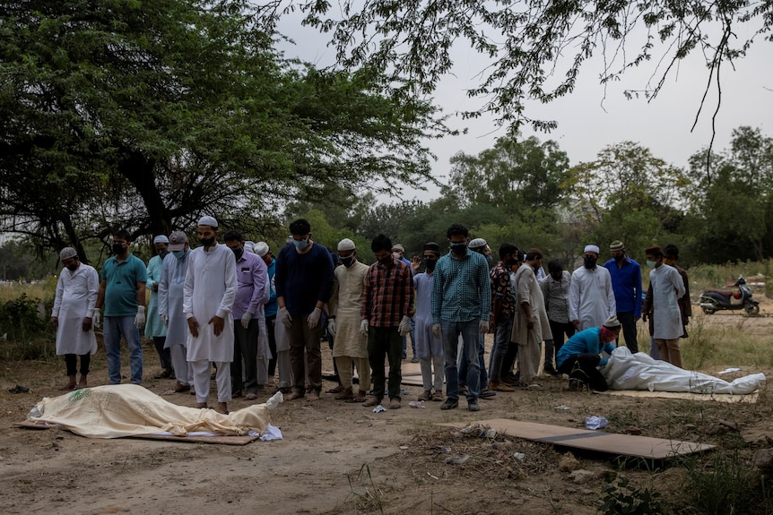 People offer prayers before burying COVID-19 victims at a graveyard in New Delhi, India.