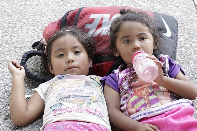 Two girls travelling on the migrant caravan rest their head on a backpack.