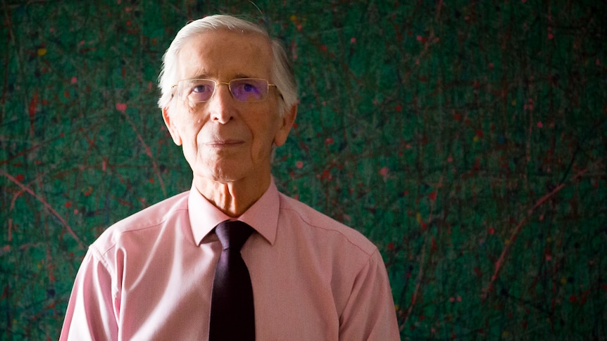 Close-up of retired judge John Nicholson standing in front of Indigenous artwork