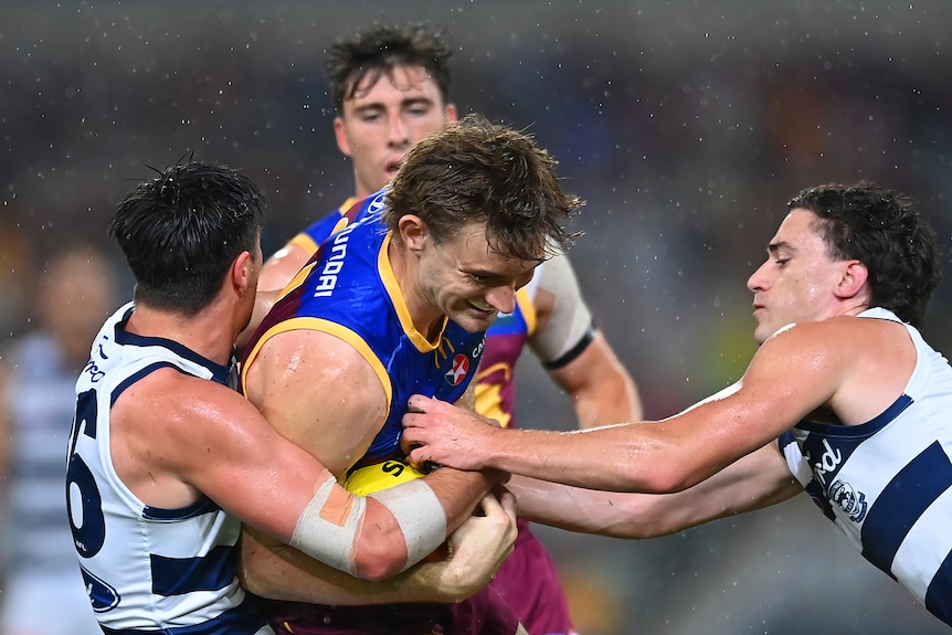 Harris Andrews grimaces while he is tackled by two Geelong players