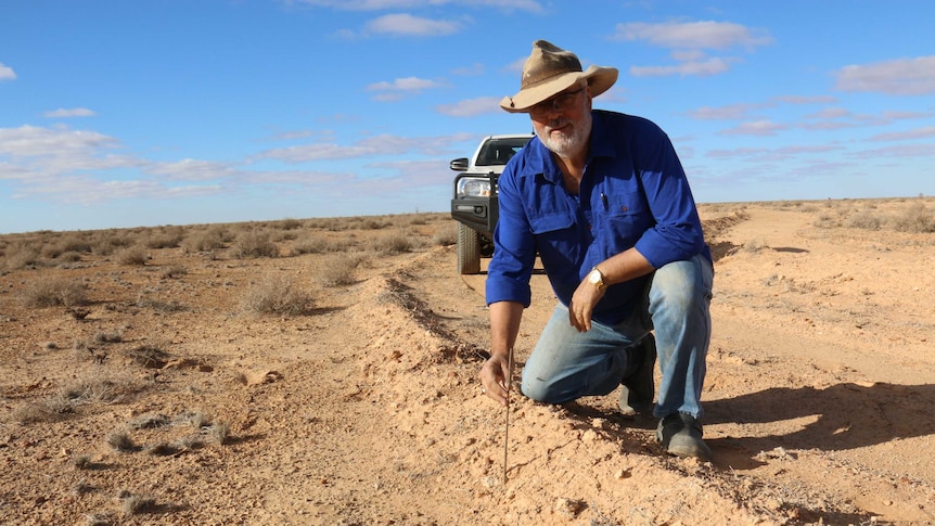 Medium shot of a man kneeling in the desert and facing the camera.