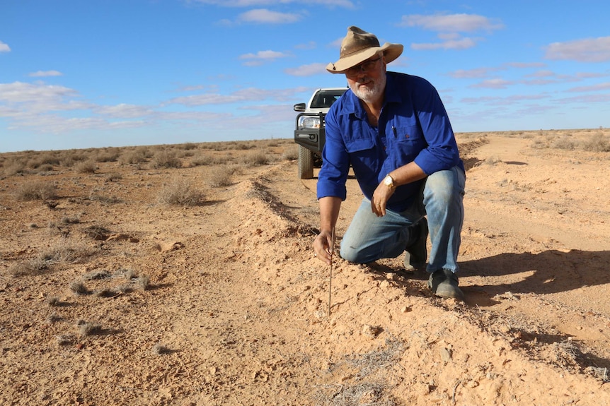 Medium shot of a man kneeling in the desert and facing the camera.