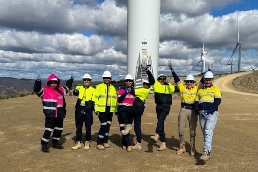 A group of women in high vis stand under a wind turbine