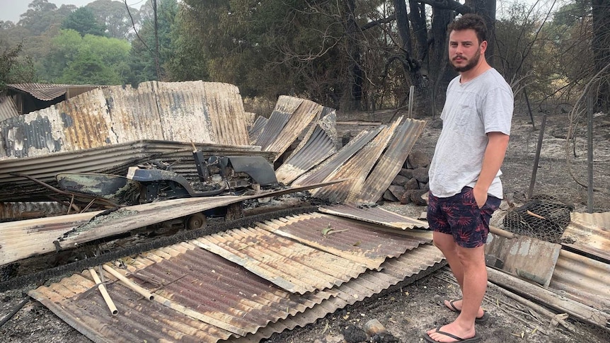 A man stands next to his burnt out home.