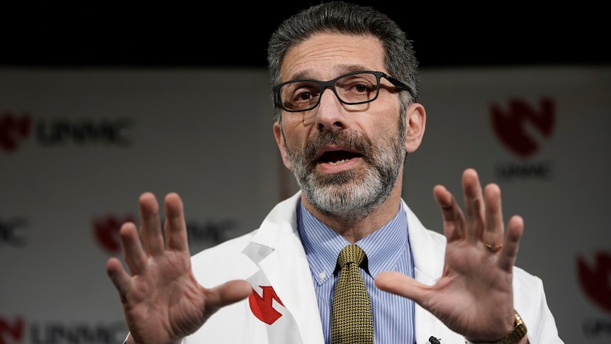 Dr Andre Kalil gesturing wearing a white coat and shirt with a tie.