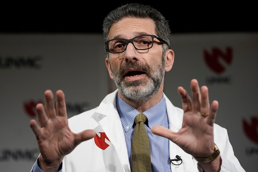 Dr Andre Kalil gesturing wearing a white coat and shirt with a tie.