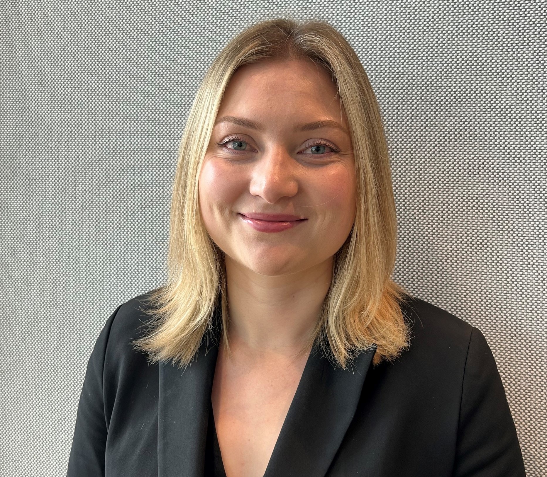 Mulher com cabelo loiro curto e jaqueta preta sorri para a câmera.