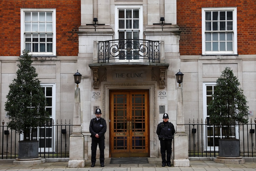 Two police officers guarding the door of a large, grand building seen from across a street.