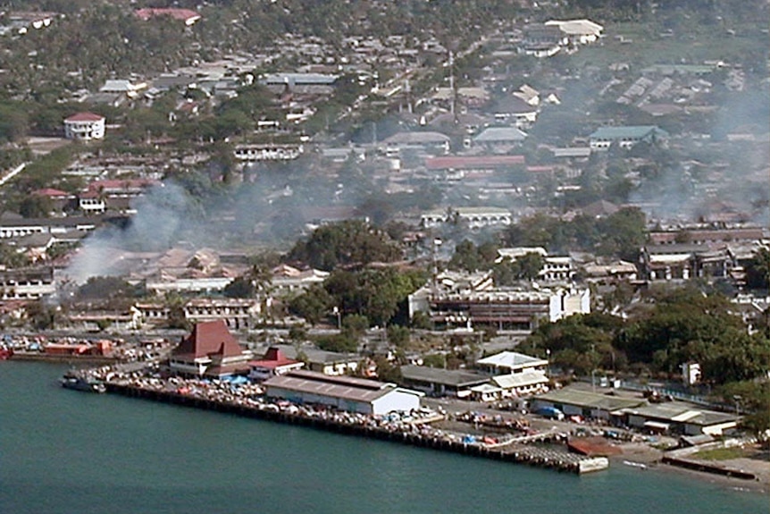 An aerial photo of a town by the sea with smoke billowing above houses