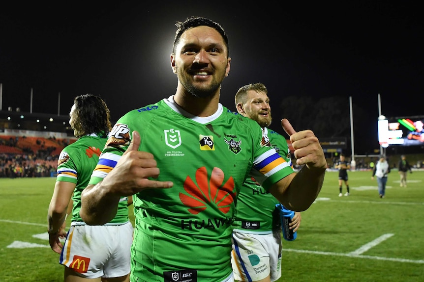 A male NRL player makes celebratory hand gestures while smiling after his team won.