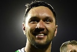 A male NRL player makes celebratory hand gestures while smiling after his team won.