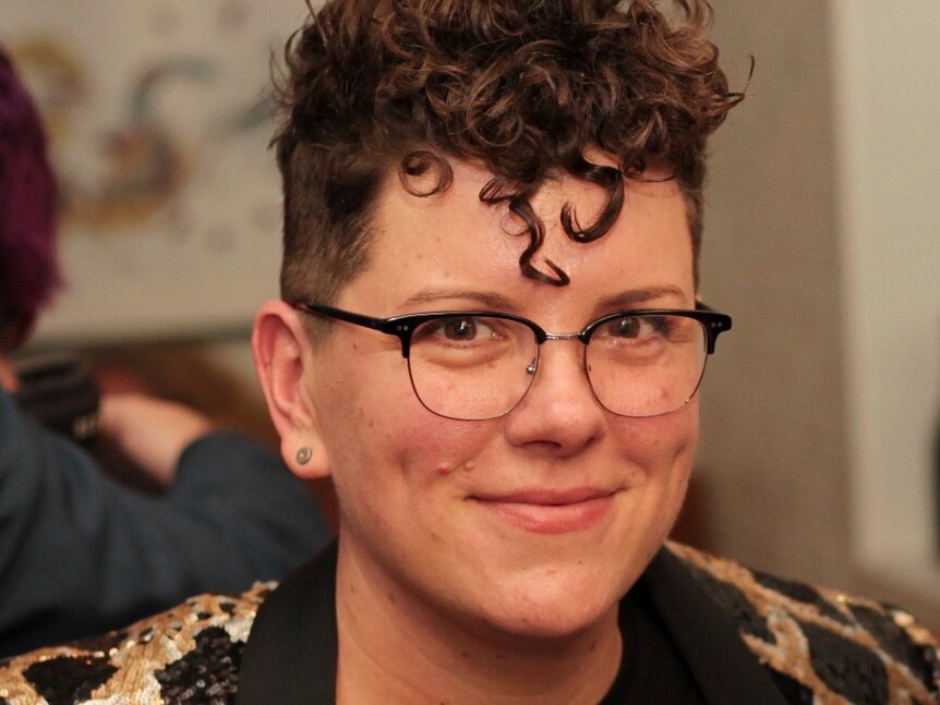 A person with curly brown hair and glasses smiles at the camera