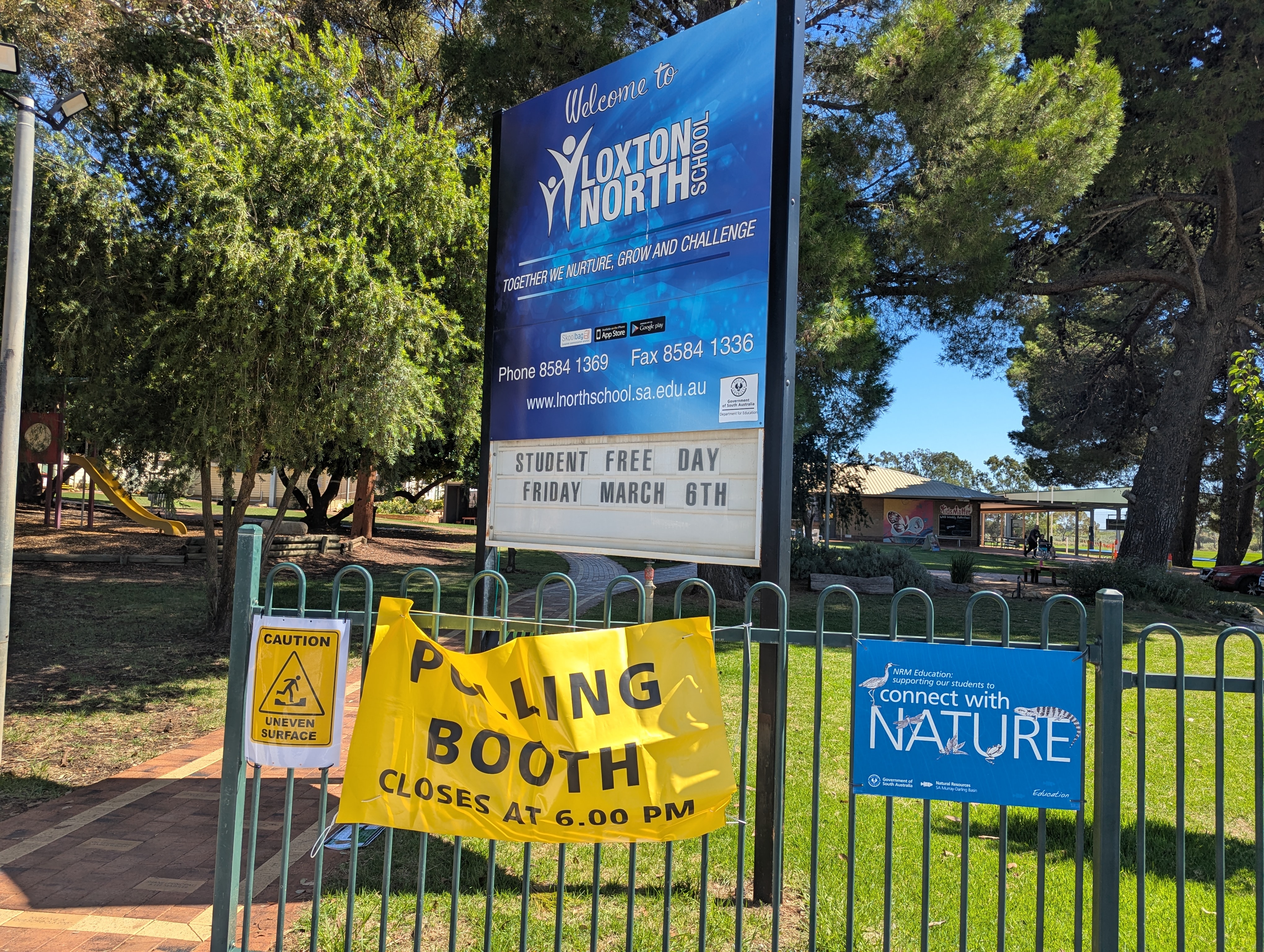 A yellow polling booth sign on a school fence